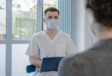 Profissional de saúde conversa com paciente durante consulta e faz anotações.