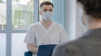 Profissional de saúde conversa com paciente durante consulta e faz anotações.