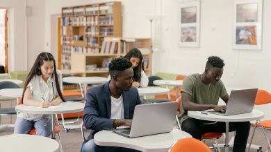 Estudantes usam laptops e fazem anotações durante uma atividade em uma sala de aula iluminada.