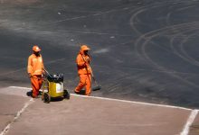 Dois trabalhadores realizam serviços de limpeza urbana em uma via de Brasília, usando uniformes laranja.