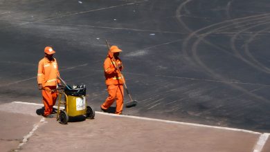 Dois trabalhadores realizam serviços de limpeza urbana em uma via de Brasília, usando uniformes laranja.