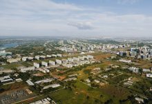 Vista aérea de Brasília, mostrando áreas urbanas, edifícios e trechos de vegetação sob a luz do dia.