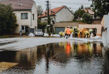 Agentes com roupas refletivas atuam em uma rua residencial alagada.