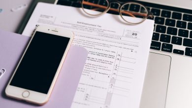 Laptop e smartphone ao lado de documentos fiscais sobre uma mesa de trabalho.