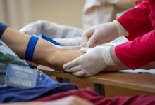 Profissional de saúde coleta sangue do braço de um doador em ambiente clínico.