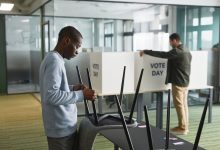 Homens preparam cabines e equipamentos de votação em um ambiente interno para o dia da eleição