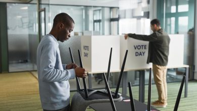 Homens preparam cabines e equipamentos de votação em um ambiente interno para o dia da eleição