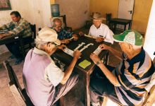 Grupo de homens idosos joga dominó em um ambiente interno de convivência.