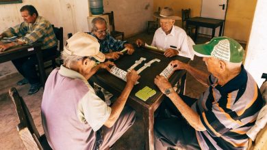 Grupo de homens idosos joga dominó em um ambiente interno de convivência.