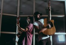 Dois músicos tocam violões em um ambiente interno durante a noite.