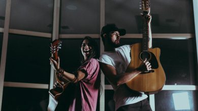 Dois músicos tocam violões em um ambiente interno durante a noite.