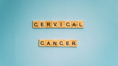 Peças de jogo de letras formam a expressão “Cervical Cancer” sobre um fundo azul-claro, em uma composição conceitual de conscientização sobre o câncer do colo do útero.