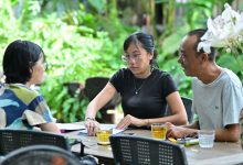 Grupo de adultos reunido em torno de uma mesa, participando de uma discussão em um ambiente arborizado.